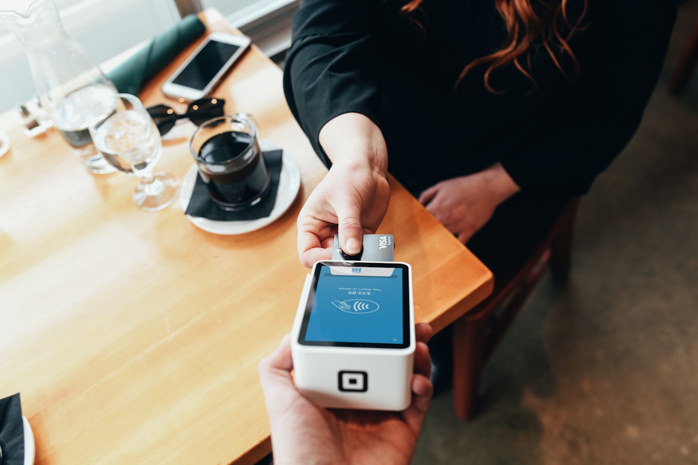 Handheld wireless credit card terminal held ready for chip, tap, or swipe in a business setting.